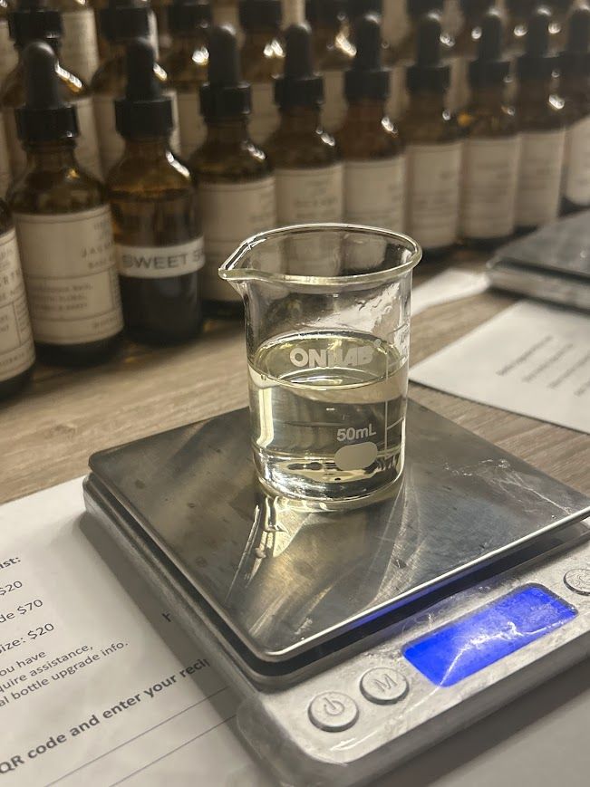 A glass beaker of fragrance oil on a bench scale, dropper bottles behind